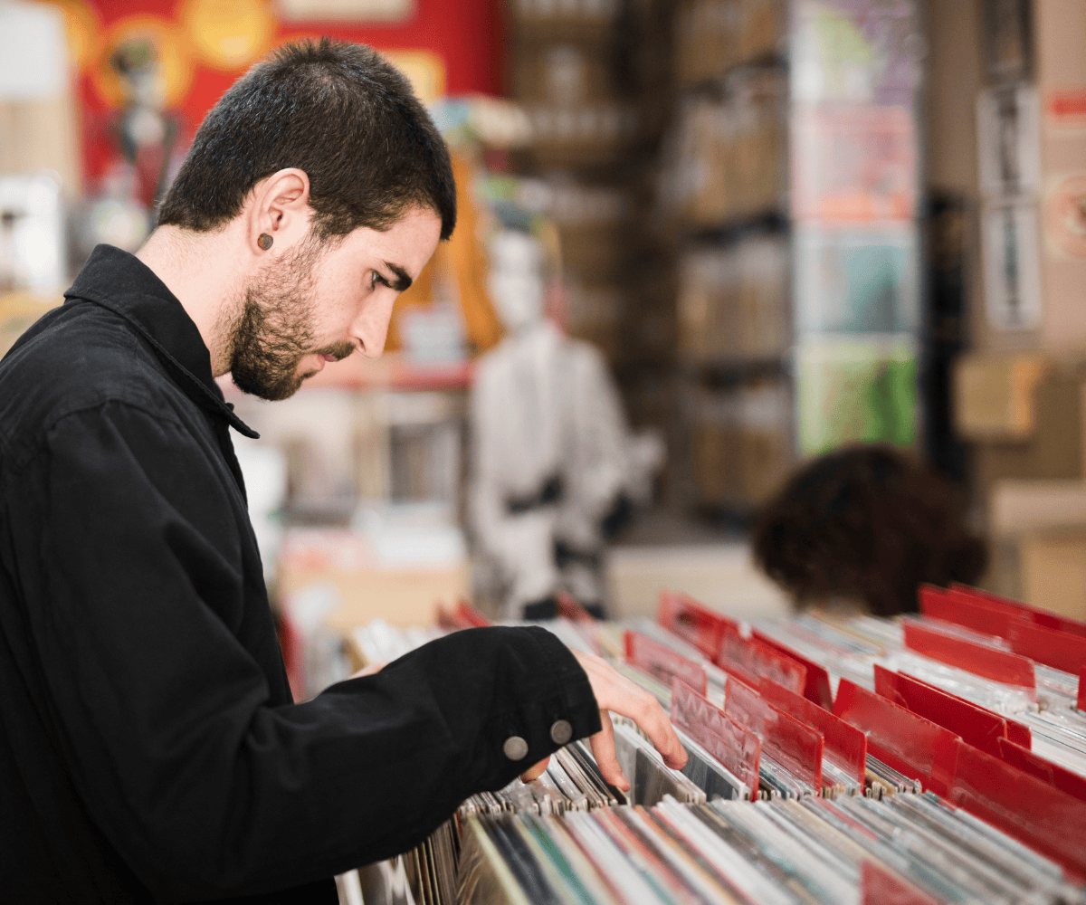 Collector browsing vinyl records in a music store, flipping through rows of albums organized in red-labeled dividers.
