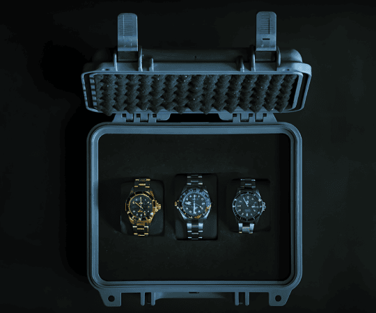 Collector’s case displaying three luxury wristwatches with metal bands, including gold, silver, and black models, secured in a protective hard case.